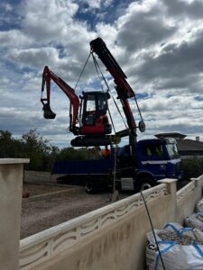 Camión con grúa elevando miniexcavadora